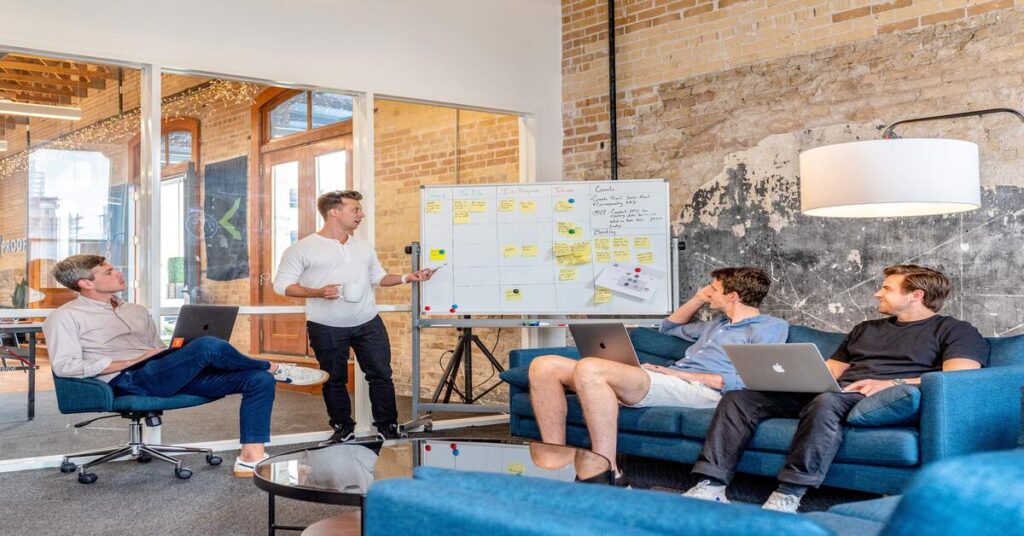 team member explaining on a white board to 3 other members sitting with laptops